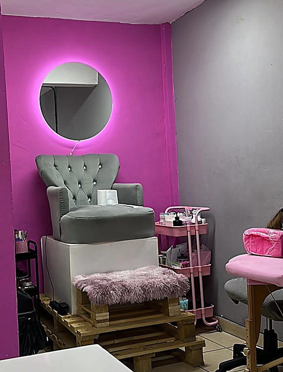 Sillón gris de capitoné sobre una tarima, bajo un espejo redondo con luz rosa en el muro magenta