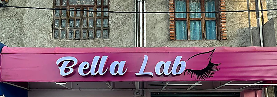 Fachada de Bella Lab: toldo fucsia con el letrero Bella Lab en cursiva blanca y una pestaña negra dibujada al final
