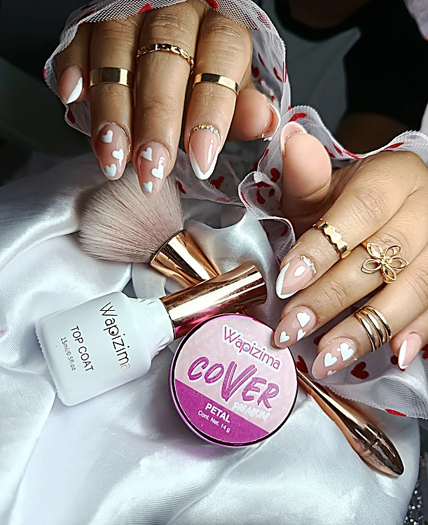 Uñas nude con corazones y flores blancas, junto a una brocha y un gel rosa