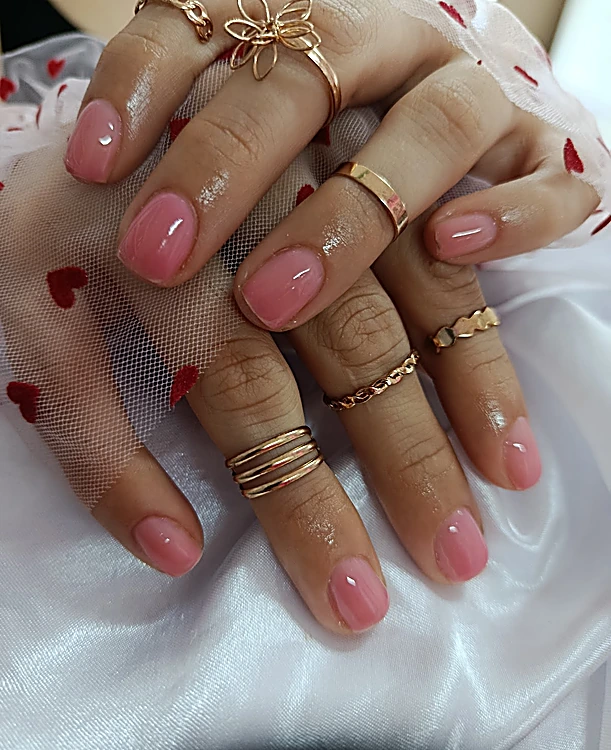 Uñas cortas en rosa translúcido con varios anillos dorados sobre tela blanca