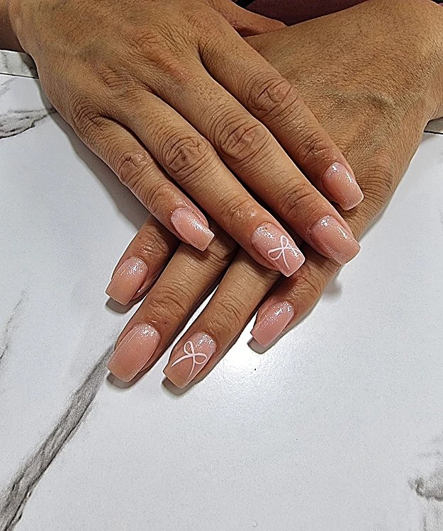Manos con uñas nude cortas y un moño blanco pintado a mano, sobre mármol blanco