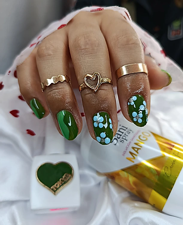Uñas verde esmeralda con flores celestes pintadas y anillo de corazón dorado